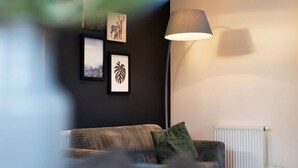 A living room with a sofa, a lamp, and framed pictures on the wall. - Pavilion 6 People XL (Zorgvlied)