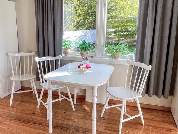 Un coin repas avec une table blanche et quatre chaises blanches, un vase rempli de fleurs et une vue sur la verdure à l’extérieur.