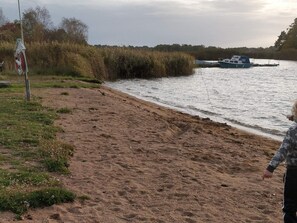 A sandy beach with a boat docked on the water, vegetation, and a person in the distance. - 3 Person Holiday Home in Ronneby (Ronneby)