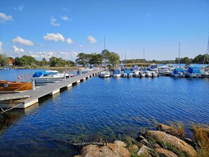 Un port de plaisance où des bateaux sont amarrés à des quais en bois, l’eau est d’un bleu limpide et l’atmosphère est paisible.