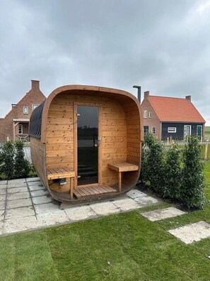 A wooden cabin with a curved roof, a glass door, and two wooden benches outside. - Villa With hot tub and Sauna, on a Holiday Park (Ossenisse)