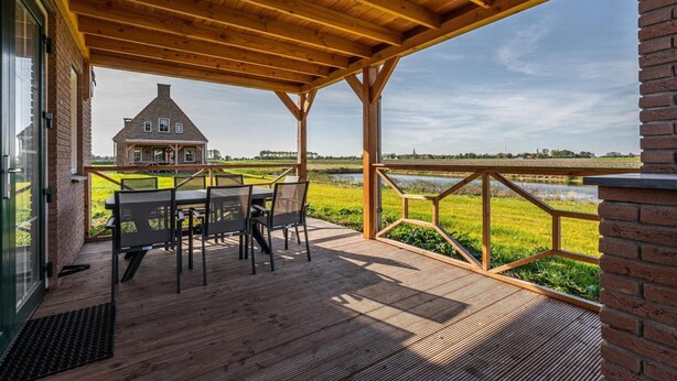 A wooden deck with a table and chairs, overlooking a large house and a body of water. - Villa With hot tub and Sauna, on a Holiday Park (Ossenisse)