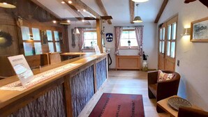 A reception area with a wooden counter, a reception desk, a wooden bench, a rug, and a coat rack. - Ferienwohnung in den Bayerischen Alpen (Bayrischzell)