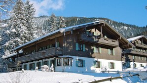 A multi-story wooden building with balconies, surrounded by snow-covered trees and mountains. - Ferienwohnung in den Bayerischen Alpen (Bayrischzell)