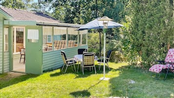 A green house with a patio area, including a table and chairs, and a covered seating area with an umbrella.
