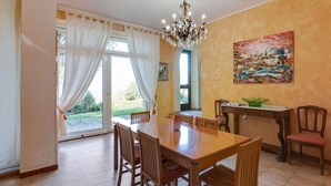 A dining area with a wooden table and chairs, a chandelier, a painting on the wall, and a view through the glass door. - Villa Near Lake Garda With Bubble Bath (Torri del Benaco)
