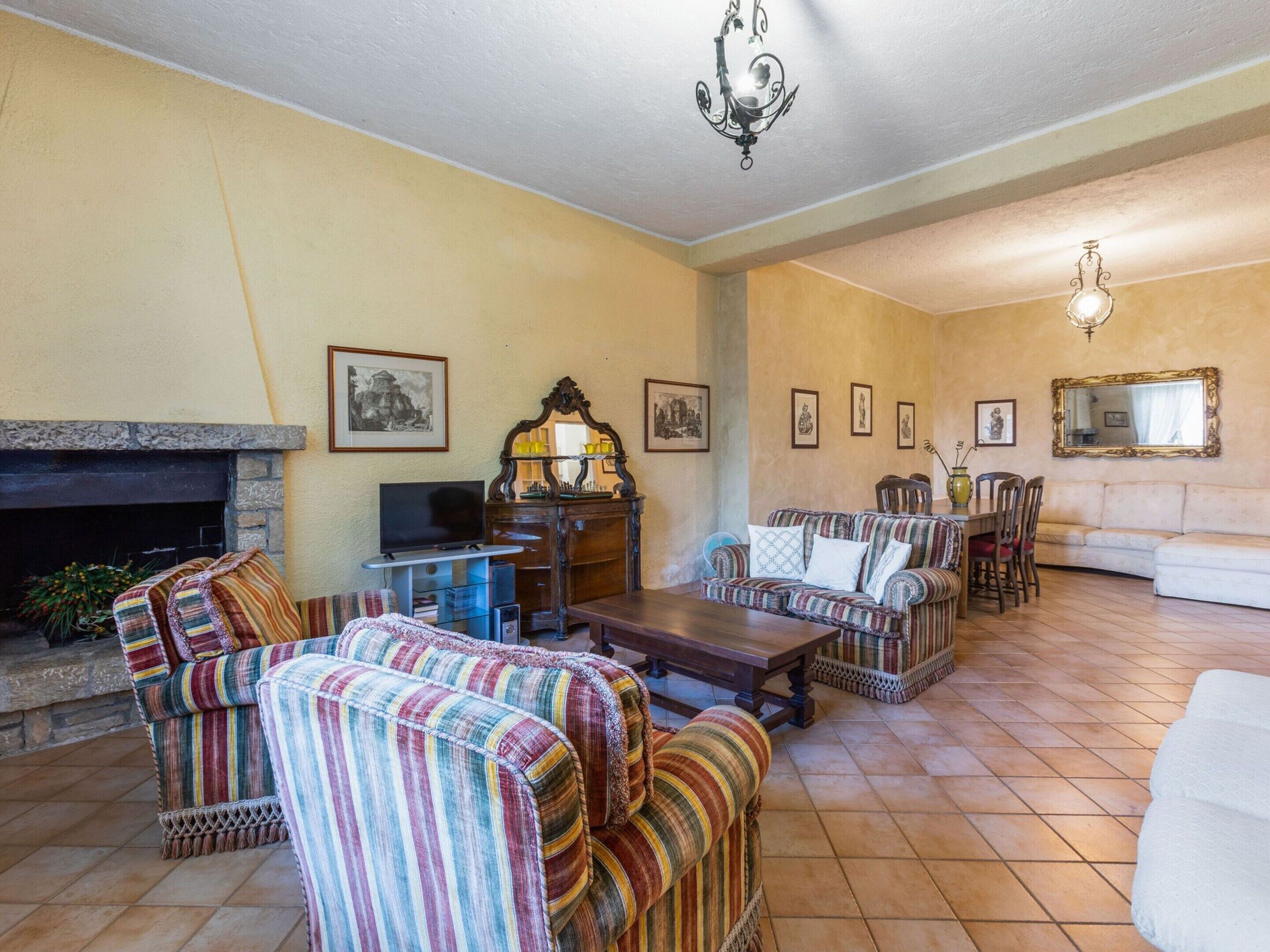 Un salon avec des canapés à rayures, une cheminée, un téléviseur et un coin repas comprenant des chaises et une table.