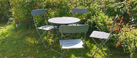 A small outdoor seating area with a round table and four chairs, surrounded by lush greenery.
