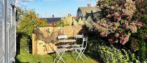 A backyard with a wooden table and chairs, a wooden fence, and various plants and flowers.