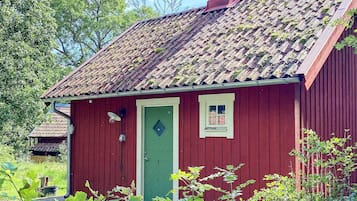 A red wooden building with a green door, a small window, and a chimney.
