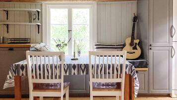 A dining area with a table and chairs, a window with a view, and a guitar leaning against a cabinet.