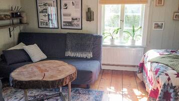 A cozy room with a sofa, a round wooden table, a patterned rug, and a bed with a quilt.