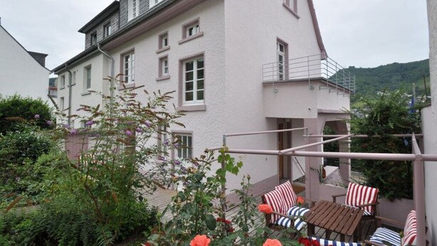 A two-story building with a balcony, surrounded by greenery and flowers. - Haus Rosa Comfortable Holiday Residence (Cochem)