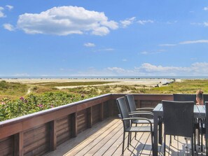 A deck with outdoor seating overlooking a beach and dunes.