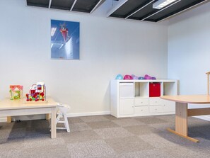 Una habitación con un escritorio blanco, una escalera pequeña, un armario blanco con cajas de almacenamiento de colores y un cuadro en la pared.