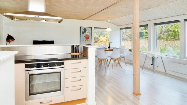 A modern kitchen with a built-in oven, a dining area with a high table and chairs, and large windows offering a view of the outdoors. - 6 Person Holiday Home in Jaegerspris (Jægerspris)