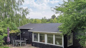 A small black cabin with a large window, a patio with a table and chairs, and a covered umbrella. - 6 Person Holiday Home in Jaegerspris (Jægerspris)
