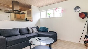 A modern living room with a grey sectional sofa, a round glass coffee table, a wooden ceiling, and a window with plants. - 6 Person Holiday Home in Jaegerspris (Jægerspris)