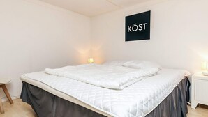 A bedroom with a bed, a nightstand, a wall-mounted sign, and a small table. - 6 Person Holiday Home in Jaegerspris (Jægerspris)