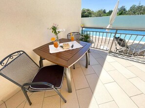 Une petite table d’extérieur avec une chaise, un verre de jus d’orange et un livre, le tout placé sur un balcon donnant sur une piscine.