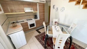 A compact kitchen with a gas stove, oven, and sink, a dining table with chairs, and a red patterned rug. - Apartment in Croatia Near Adriatic Coast (Crikvenica)