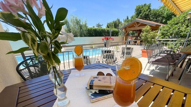 A table with drinks, a book, and a vase of flowers on a balcony overlooking a pool. - Apartment in Croatia Near Adriatic Coast (Crikvenica)
