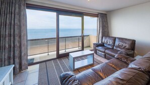 A modern living room with a leather sofa, a glass coffee table, and a view of the sea through large sliding doors. - Bright Apartment Near the Center (Middelkerke)