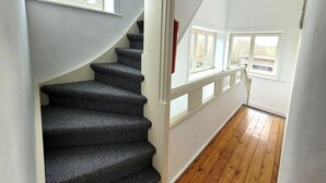 Una escalera con alfombra texturizada, paredes blancas y suelo de madera.