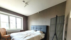 Un dormitorio con una cama grande, una ventana, un radiador y una silla.