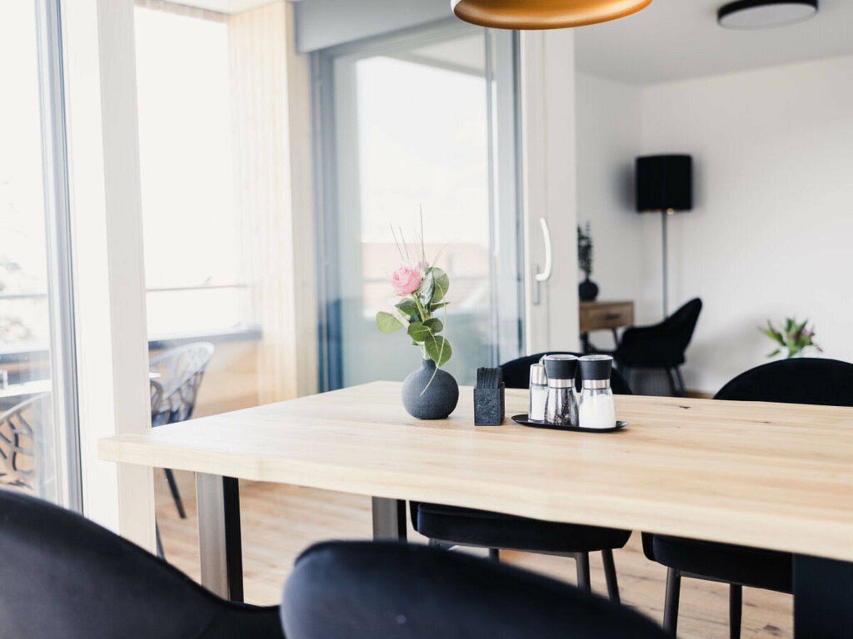 A modern dining area with a wooden table, black chairs, a vase with flowers, and a coffee maker.