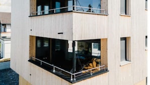 Un immeuble moderne à plusieurs étages, doté d’une façade en bois, de grandes fenêtres et d’un balcon situé à l’étage supérieur.