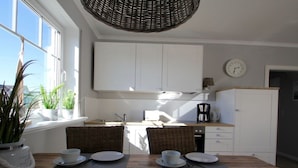 A modern kitchen with white cabinets, a dining table set for four, and a large window with plants. - "isabel" in the House to the cog (Zingst)