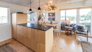 A spacious kitchen with wooden cabinets, a black countertop, pendant lighting, and a dining area with white chairs and a table. - 4 Person Holiday Home in Fano (Fano)