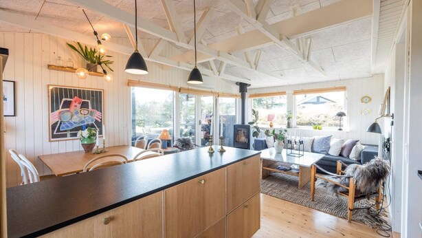 A spacious kitchen with wooden cabinets, a central island, pendant lighting, and a large window overlooking a garden. - 4 Person Holiday Home in Fano (Fano)