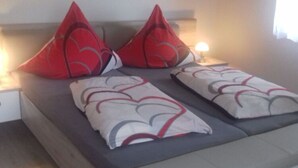 A bed with grey bedding and red pillows, a bedside table with a lamp, and a window with curtains.