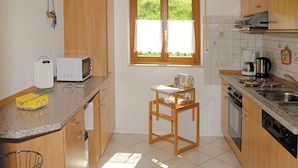 A compact kitchen with wooden cabinets, a microwave, a toaster, a sink, and a window with curtains.