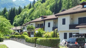Une rangée de bâtiments blancs aux toits bruns, entourés d’une végétation luxuriante et avec des montagnes en arrière-plan.