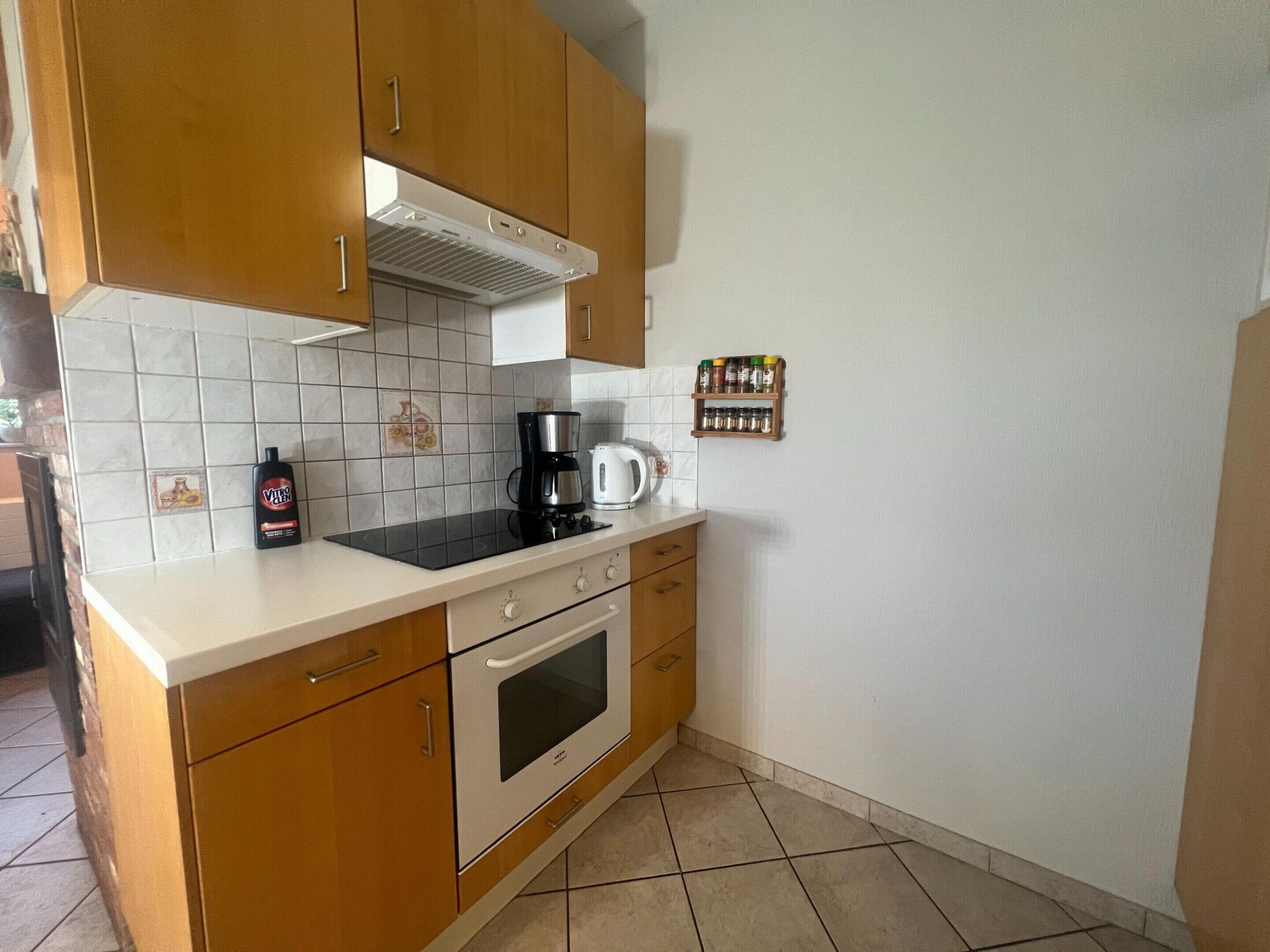 A kitchen with wooden cabinets, a white countertop, a stove, a coffee maker, and a spice rack.