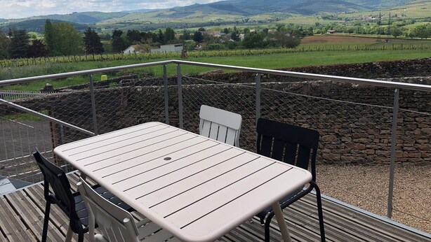 Eine Terrasse mit Tisch und Stühlen, mit Blick auf eine ländliche Landschaft mit Feldern und Hügeln.