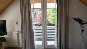 A room with a wooden ceiling, a sliding glass door to a balcony, a radiator, a treadmill, and a potted plant.