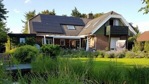 A house with a sloped roof, solar panels, a covered patio, and a garden with tall grasses.