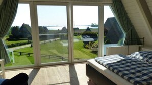 Ein Schlafzimmer mit einem großen Schiebeglasfenster, das einen Blick auf einen Golfplatz und ein Gewässer freigibt.