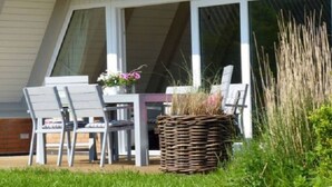 Eine Terrasse im Freien mit Tisch und Stühlen, einem Korbwägelchen und einer kleinen Gartenanlage mit Pflanzen.