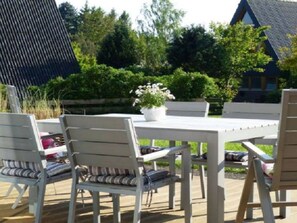 An outdoor seating area with a white table and chairs, surrounded by greenery and a house in the background. - Holiday Home Sehnsucht Schlei (Brodersby)