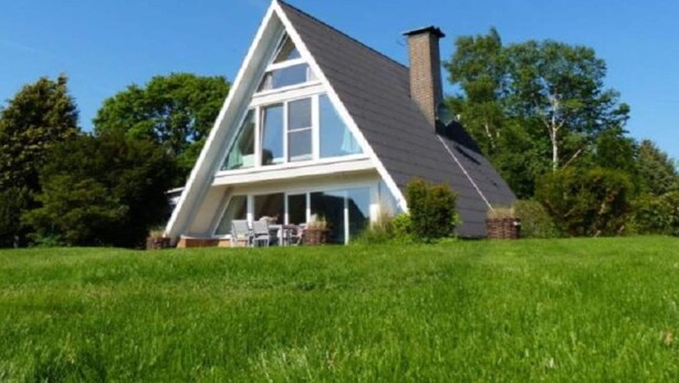 Ein modernes Haus mit einem dreieckigen Dach, großen Fenstern und einem Schornstein.