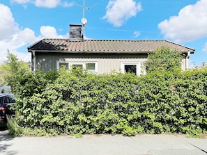 Una casa de dos pisos con antena parabólica, chimenea y un seto en la fachada.