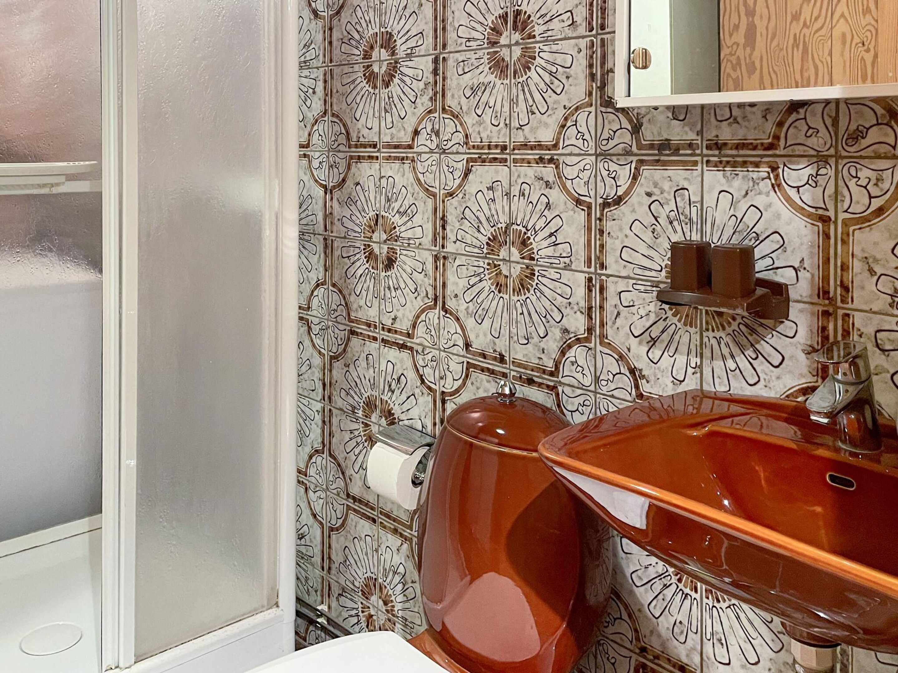A bathroom with a patterned tile backsplash, a white toilet, and a brown sink with a mirror above it.
