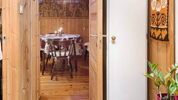A wooden interior with a dining table set for two, a potted plant, and a door leading to another room.