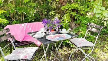 An outdoor dining area with a table set for two, surrounded by greenery.