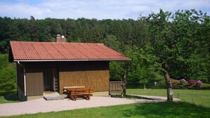 A small, single-story building with a tiled roof and a wooden bench outside. - 2 Siefertshof Comfortable Holiday Residence (Mossautal)